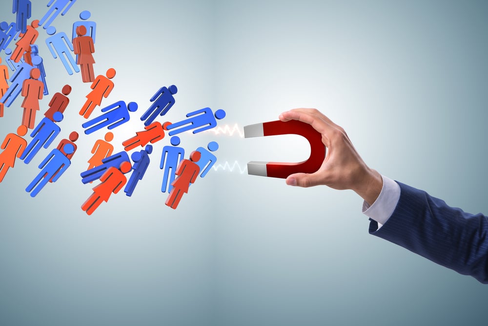 A mão de um homem segura um ímã que atrai pessoas em formato de bonecos, simbolizando como as estratégias para retenção de talentos funcionam.