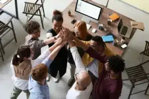 Grupo diverso de profissionais unidos em um gesto de trabalho em equipe, refletindo uma cultura saudável em pequenas e médias empresas