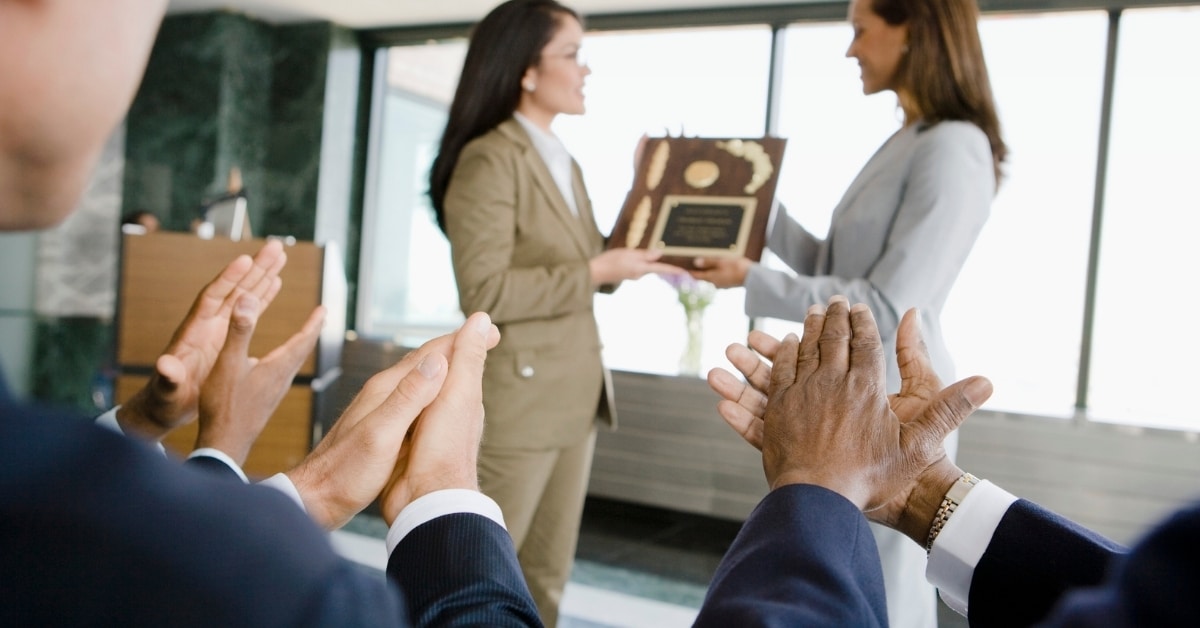 mulher recebendo premiações da chefe com 3 pessoas aplaudindo