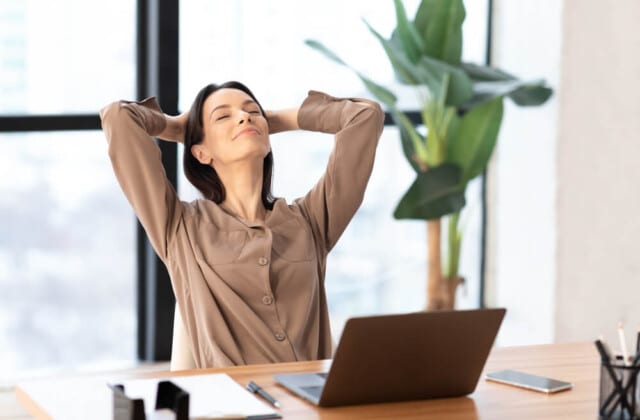 Uma mulher de blusa bege se recosta na cadeira com as mãos atrás da cabeça, personificando a essência da saúde mental no trabalho.