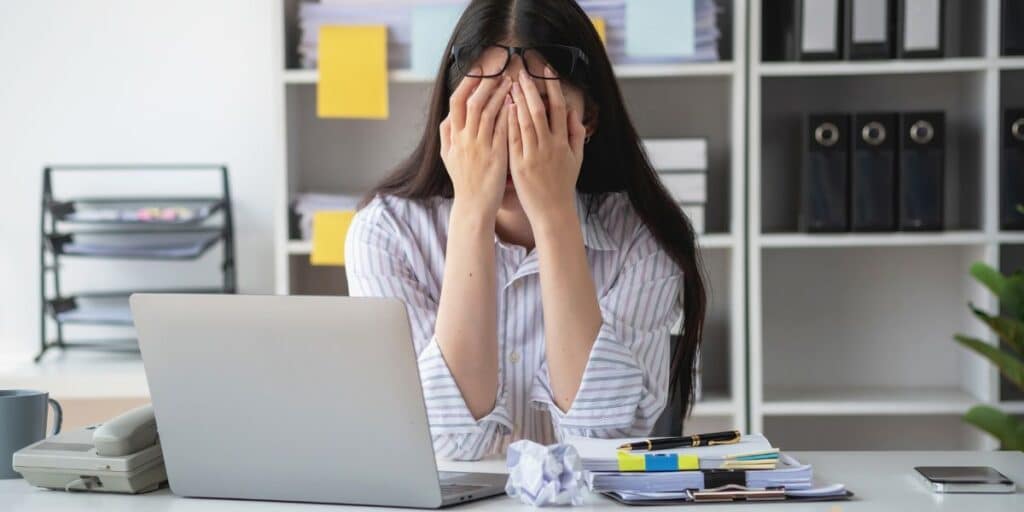 mulher com a mão no rosto na mesa de trabalho representando que burnout agora é doença mental