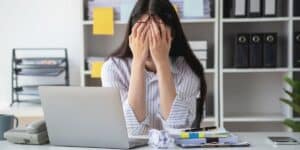 mulher com a mão no rosto na mesa de trabalho representando que burnout agora é doença mental