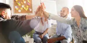 colaboradores de uma empresa estão sentados em uma roda e batendo as mãos em conjunto no alto, para comemorar as aplicações de estratégias de endomarketing de sucesso, o que gera um time produtivo e engajado na empresa