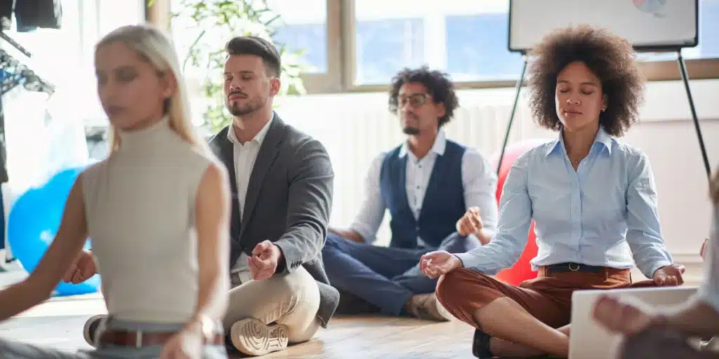 colaboradores sentados no chão fazendo um exercício de meditação em uma empresa que se preocupa com a saúde mental das pessoas, colocando em prática e seguindo a NR-01