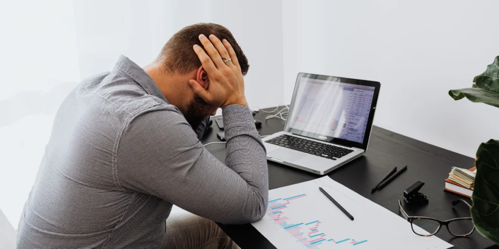 homem estressado no escritorio diante de notebook e graficos