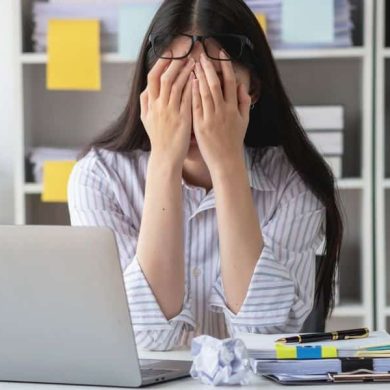 mulher com a mão no rosto na mesa de trabalho representando que burnout agora é doença mental