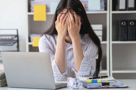 mulher com a mão no rosto na mesa de trabalho representando que burnout agora é doença mental