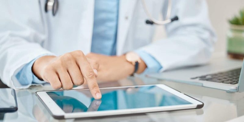 Médico de jaleco usa tablet na mesa, simbolizando o futuro na saúde digital com tecnologia e inovação nos cuidados médicos