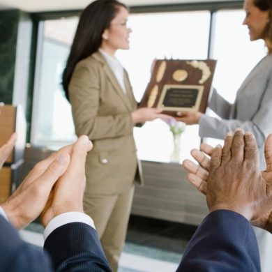 mulher recebendo premiações da chefe com 3 pessoas aplaudindo