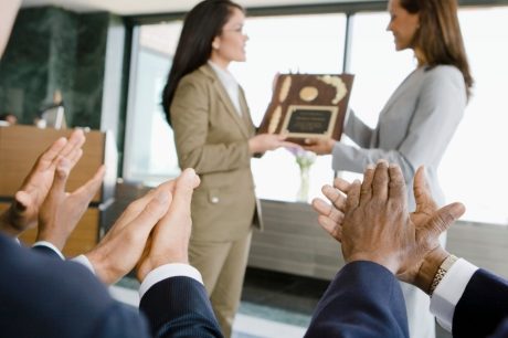 mulher recebendo premiações da chefe com 3 pessoas aplaudindo