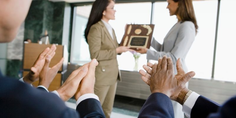 mulher recebendo premiações da chefe com 3 pessoas aplaudindo