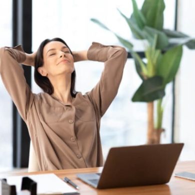 Uma mulher de blusa bege se recosta na cadeira com as mãos atrás da cabeça, personificando a essência da saúde mental no trabalho.